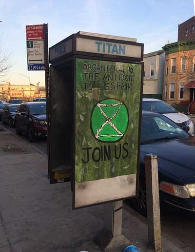 "Organizing is the antidote to despair - Join Us" is painted on a poster with a symbol for climate change at a city bus stop.