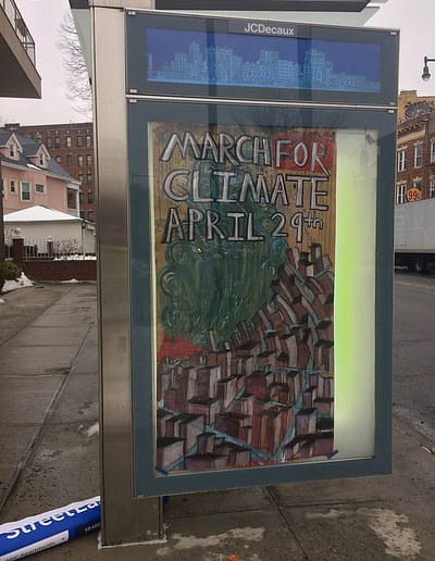 A city bus stop shelter ad box advertises a March for Climate Action with an image of a burning city.