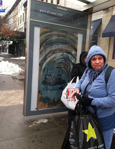 On a winter day a woman in a sweatshirt holds full bags as she stands in front of an ARRT! poster protesting deportations.